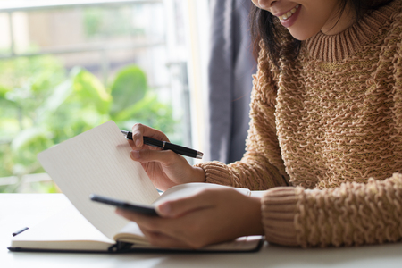 Close-up of smiling lady reading her notes in diary. Positive young woman sitting at table and planning timetable. Schedule conceptの写真素材