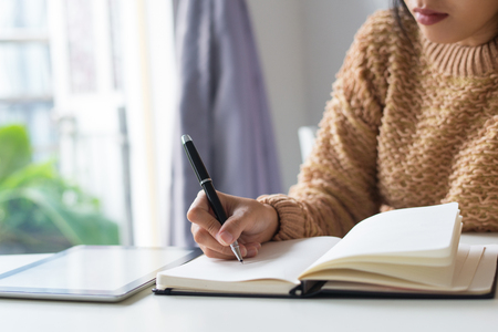Close-up of pensive woman writing out ideas in diary. Busy woman sitting at table and making notes. Timetable conceptの写真素材