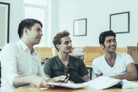 Group of excited trainees watching presentation. Three smiling young men at classroom desk looking at virtual wall display. Presentation conceptの写真素材