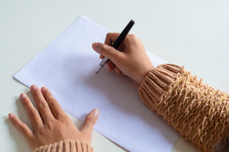Close-up of woman in fluffy sweater sitting at table and making notes. Unrecognizable lady analyzing report. Planning conceptの写真素材