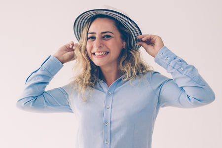 Happy attractive lady putting on sun hat and smiling at camera. Cheerful playful woman in blouse adjusting hat. Fashion accessory conceptの写真素材