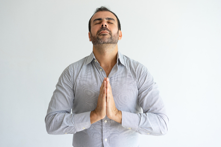 Peaceful man praying with his eyes closed. Handsome guy keeping hands together and dreaming about something. Prayer concept. Isolated front view on white background.の写真素材