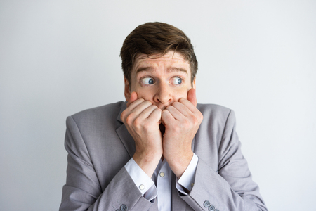 Desperate and scared businessman keeping silence. Concerned young Caucasian man covering mouth with hands and looking away. Fear or panic conceptの写真素材