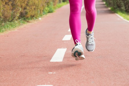 Close-up of female runner practicing outdoors. Woman in gray sport shoes and pink leggings jogging...
