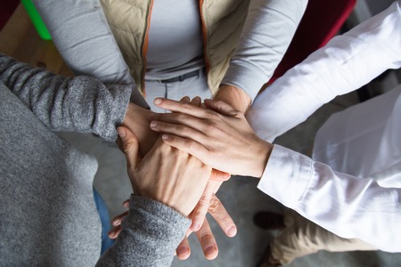 Team showing unity. Closeup top view of three young people putting their hands together. Cooperation...
