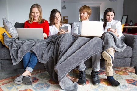Group of students working on their home assignment. Four young people sitting on couch together...