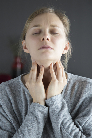 Sick young fair-haired Caucasian woman with closed eyes having sore throat, touching her neck. Illness, pain conceptの写真素材