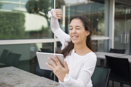 Portrait of happy young woman taking selfie with digital tablet. Caucasian girl winking and showing winning gesture at pc tablet. Social networking conceptの写真素材