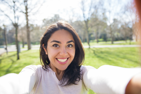 Selfie of smiling excited girl walking outdoors. Happy joyful young woman taking picture of herself in city park. Euphoria conceptの写真素材