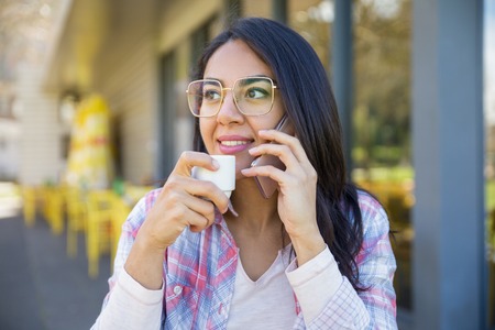 Positive smart student girl resting in street coffee shop. Young woman wearing glasses and casual...