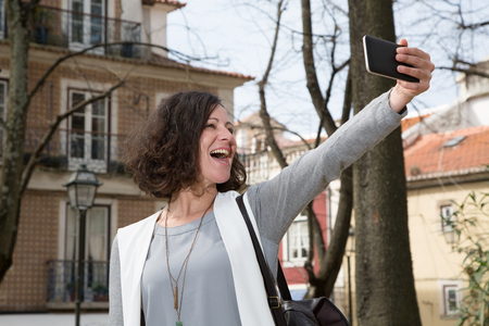 Excited tourist enjoying leisure time in historic district. Overjoyed lady smiling at smartphone camera and taking selfie. Happy tourist conceptの写真素材