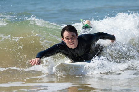 Excited handsome man swimming on surfboard in sea. Young guy wearing wetsuit, lying on board and rowing with hands. Surfboarding and vacation concept. Front view.の写真素材
