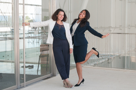 Two joyful female colleagues standing in office hall. Women looking at camera, standing and dancing. Break and joy concept. Front view.の写真素材