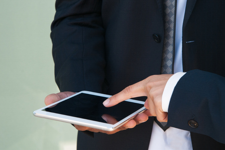 Closeup of tablet with blank screen in hands of man. Two business colleagues using gadget together. Teamwork or communication conceptの写真素材