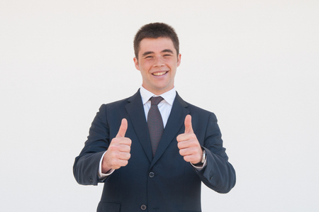 Cheerful young professional expressing approval. Young man in office jacket and tie showing thumbs up and smiling at camera. Like gesture or approval conceptの写真素材