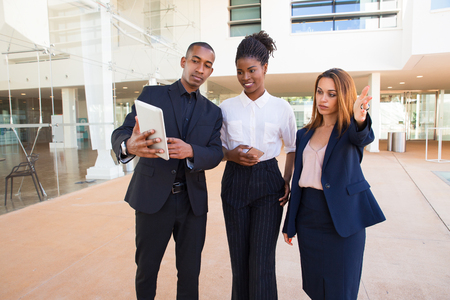 Black manager showing sketch on tablet to young ladies while asking question. Serious redhead woman pointing straight with hand. Planning startup project conceptの写真素材