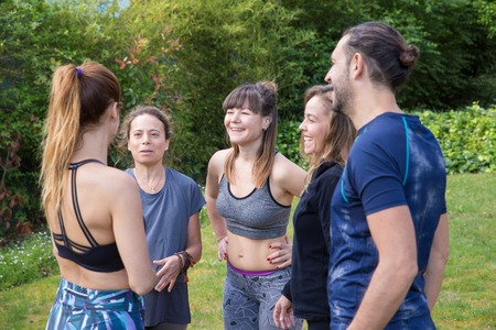 Team of positive yogis chatting in park. Man and women in fitness apparels standing outdoors and talking. Yoga and communication conceptの写真素材