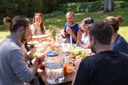 Portrait of serious young people having brunch outdoors. Friends or family eating at table outdoors....
