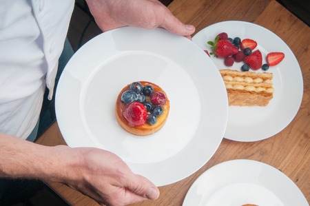 Waiter bringing fruit dessert. Above view of unrecognizable man holding plate with delicious cake...