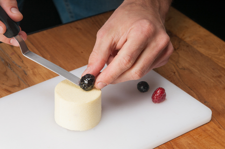 Closeup of man putting berry on peace of ice-cream at table. Guy using spatula, frozen blueberries and raspberry on cutting board on wooden table. Dessert and culinary concept.の写真素材