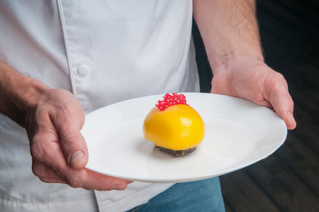 Close-up of man holding beautiful colorful dessert. Unrecognizable chef presenting new sweet dish in restaurant. Recipe conceptの写真素材