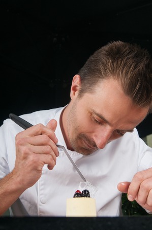 Positive chef decorating ice-cream with berries. Man holding spatula and putting blueberries and raspberry on piece of ice-cream at table. Dessert and culinary concept. Front view.の写真素材