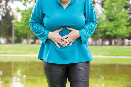 Woman suffering from belly ache. Plus sized lady standing in park and touching stomach. Health problem conceptの写真素材