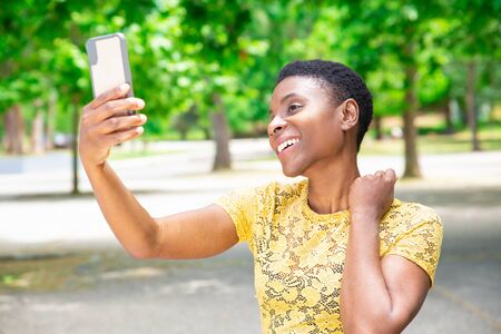 Beautiful African-American woman taking selfie in park. Attractive young Black woman in lace blouse...