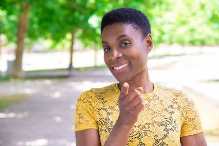 Smiling confident black woman pointing with finger at camera. Successful young lady in yellow tshirt choosing you. Appeal conceptの写真素材