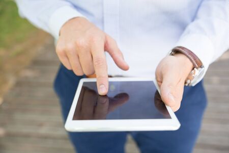 Businessman wearing striped shirt and wristwatch using tablet outdoors. Closeup of male hands...