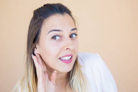 Excited curious lady hearing secret news or gossips. Young woman in casual keeping hand at ear and listening carefully. Curiosity conceptの写真素材