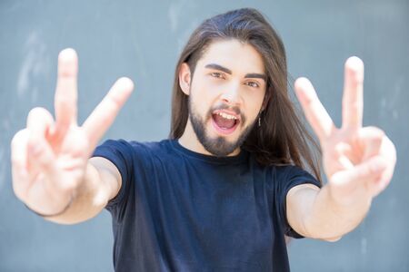 Positive young man shouting and making victory gesture. Portrait of brunet with nose ring and...
