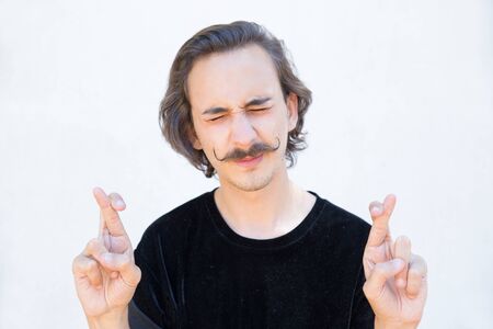 Worried man with handlebar mustache holding cross fingers. Stylish brunet gesturing. Concept of good...