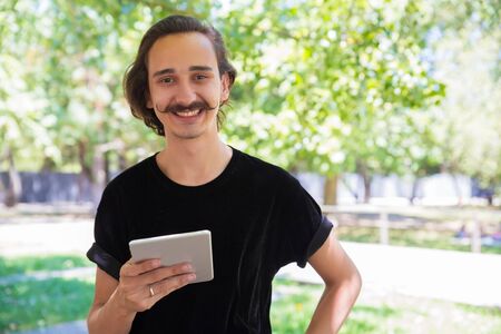 Happy man with tablet pc outdoor. Cheerful young man holding digital tablet and smiling at camera in...
