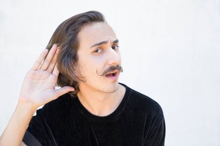 Deaf man with mustache cupping hand behind ear. Handsome young guy cant hear. Deafness concept