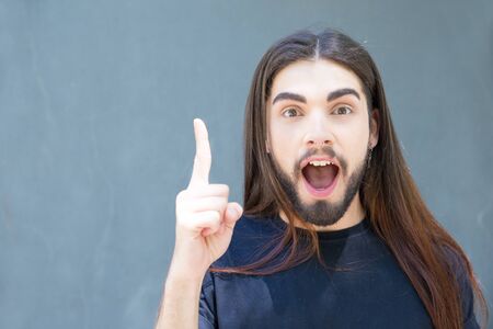 Excited young brunet man pointing upward with finger. Emotional guy with piercing gesturing outdoor....