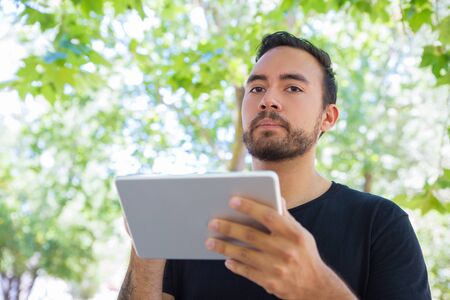 Bearded man using tablet pc outdoor. Low angle view of handsome young man holding digital tablet. Wireless technology conceptの写真素材