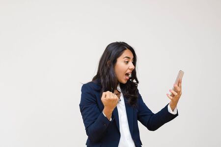 Emotional young businesswoman using smartphone. Professional young businesswoman in formal wear holding mobile phone isolated on grey background. Connection conceptの写真素材