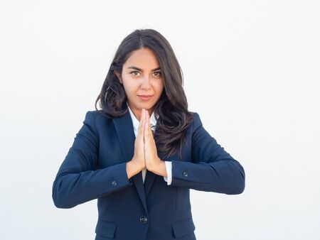 Serious calm businesswoman making Namaste gesture. Young Latin woman in office suit practicing meditation. Stress relief conceptの写真素材