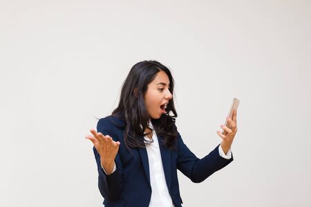 Shocked young businesswoman using smartphone. Emotional young businesswoman in formal wear using cell phone isolated on grey background. Technology conceptの写真素材