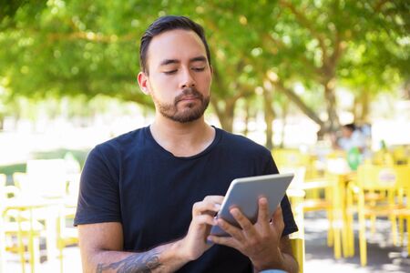 Handsome man using digital tablet outdoor. Bearded young man standing and using tablet pc in park. Wireless technology conceptの写真素材