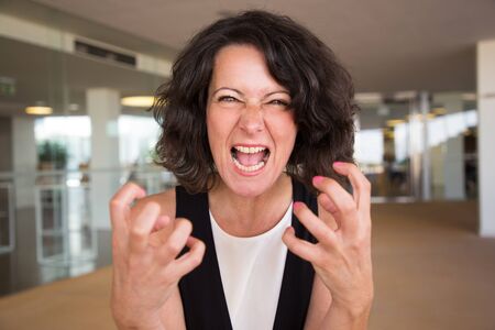 Crazy furious woman shouting at camera. Angry middle aged lady in casual screaming, making claw gesture and aggressive grimace. Aggression conceptの写真素材