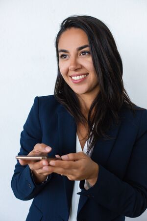 Smiling young woman holding mobile phone. Beautiful happy young businesswoman using smartphone and looking away isolated on grey background. Technology conceptの写真素材