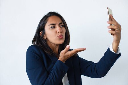 Attractive young businesswoman using smartphone. Beautiful young woman blowing kiss and pouting lips during video call via cell phone. Communication conceptの写真素材