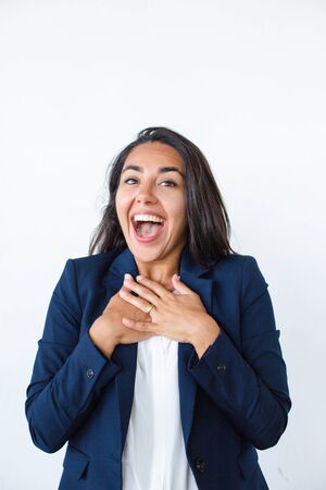 Surprised young businesswoman. Beautiful cheerful young woman in formal wear holding hands on chest and smiling at camera. Emotion conceptの写真素材