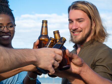 Smiling friends cheering with beer bottles in park. Group of young people relaxing after work. Celebration conceptの写真素材