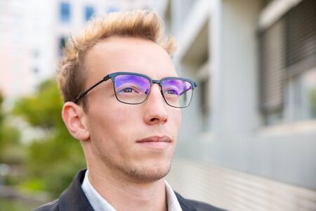 Confident business leader in glasses looking into distance. Closeup of pensive handsome young man in eyeglasses staring away. Business portrait conceptの写真素材