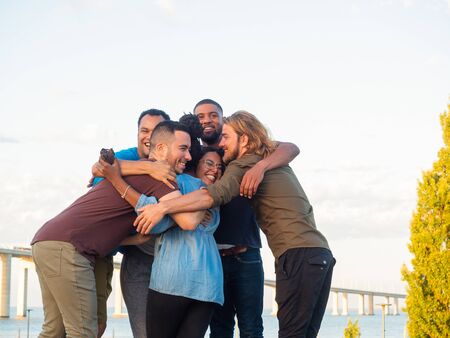 Happy friends standing in circle and hugging in park. Group of smiling young people standing in...