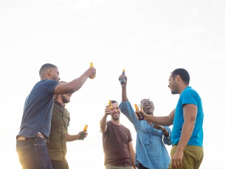 Relaxed people standing with beer bottles. Group of friends relaxing in park during sunset. Leisure...