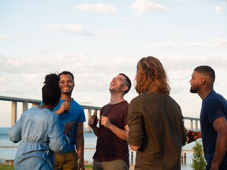 Smiling people having fun together during summer party. Young friends laughing while drinking beer...